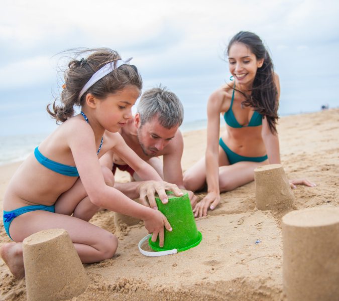 A six year old is bulding a sand castle with her parents. Focus on the girl
